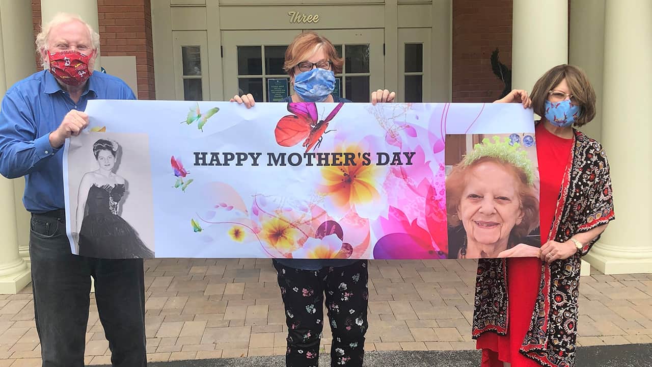 Photo of Steve Turner and his sisters, Carla Paull and Lisa Fishman, holding up a Mother’s Day banner 