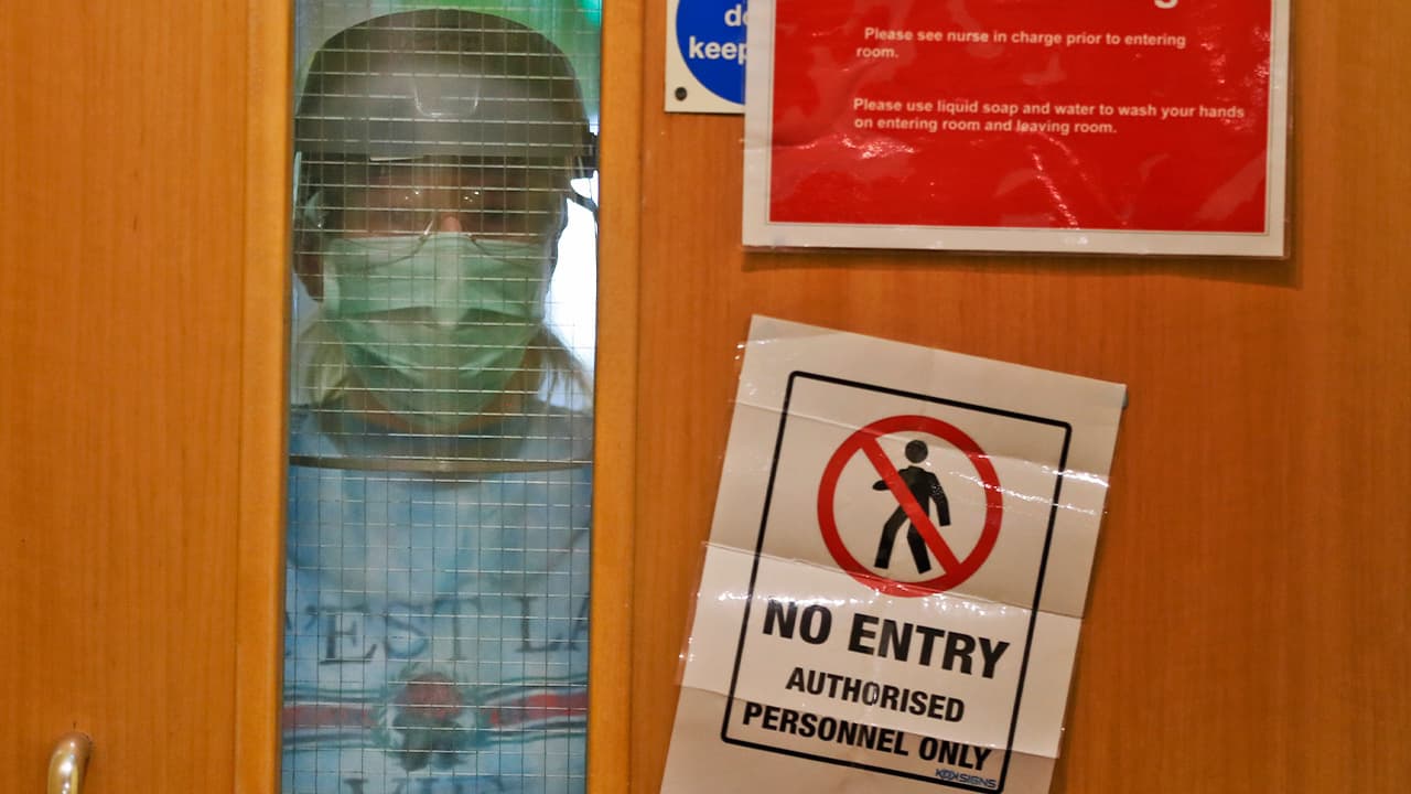 Photo of a nurse wearing PPE looks through a window of a closed door