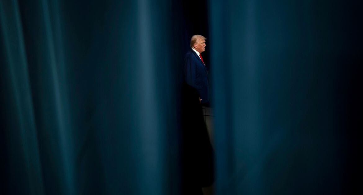 Trump seen through stage curtains.