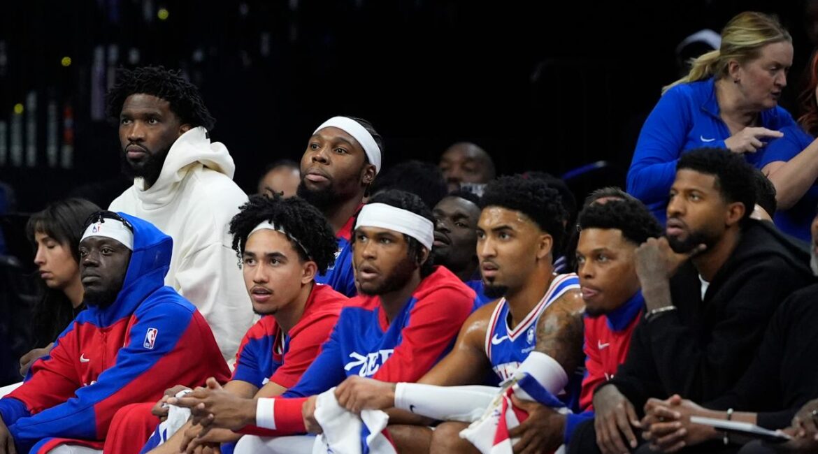 Philadelphia 76ers' Joel Embiid, top left, and Paul George, bottom right, watch from the bench during the first half of an NBA basketball game against the Milwaukee Bucks, Wednesday, Oct. 23, 2024, in Philadelphia. (AP Photo/Matt Slocum)