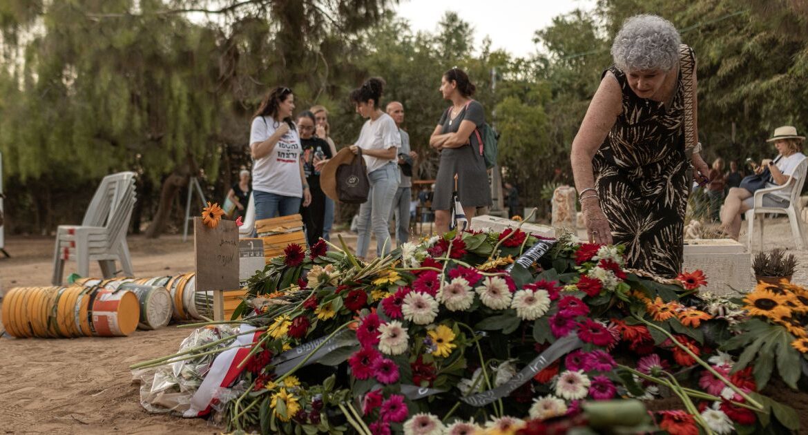 Ruti Munder reaches out to touch the flowers covering the grave of her husband, Israeli hostage Avraham Munder, during his funeral at Kibbutz Nir Oz, in southern Israel, Aug. 21, 2024. Six Israeli hostages whose bodies were found in Gaza over the summer were probably shot dead by their Hamas captors in February, around the same time that an Israeli airstrike hit near the underground tunnel where they were being held, the Israeli military said on Wednesday, Dec. 4, 2024. (Avishag Shaar-Yashuv/The New York Times)