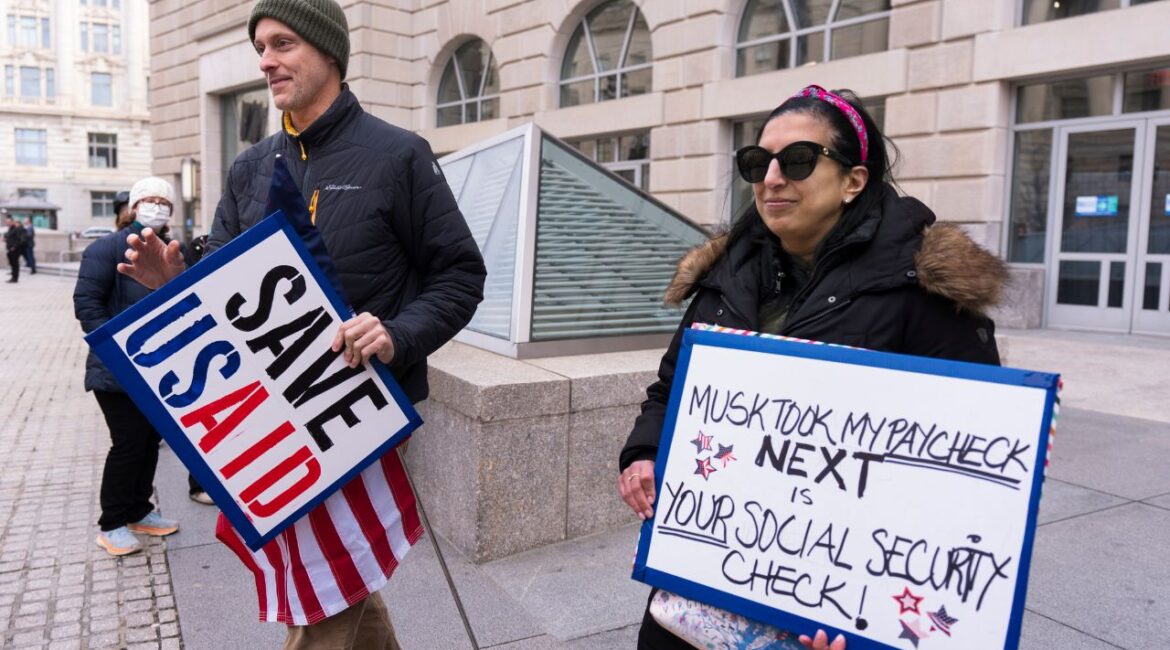 United States Agency for International Development, or USAID contract worker Priya Kathpal, right, and Taylor Williamson, left, who works for a company doing contract work for USAID, carry signs outside the USAID headquarters in Washington, Monday, Feb. 10, 2025. (AP Photo/Manuel Balce Ceneta)