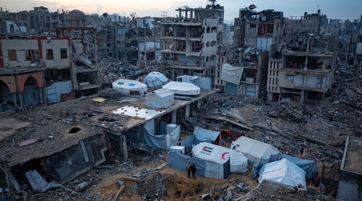 Palestinians stand next to tents surrounded by buildings that were destroyed by the Israeli air and ground offensive in Jabaliya, Gaza Strip, Tuesday, Feb. 11, 2025. (AP/Jehad Alshrafi)