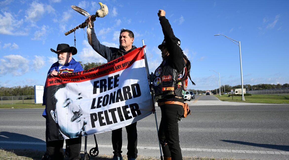 Supporters Mike McBride, left, Ray St. Clair, center, and Tracker Gina Marie Rangel Quinones stand in front of Federal Correctional Complex, Coleman, while awaiting the release of Leonard Peltier, Tuesday, Feb. 18, 2025, in Sumterville, Fla. (AP/Phelan M. Ebenhack)