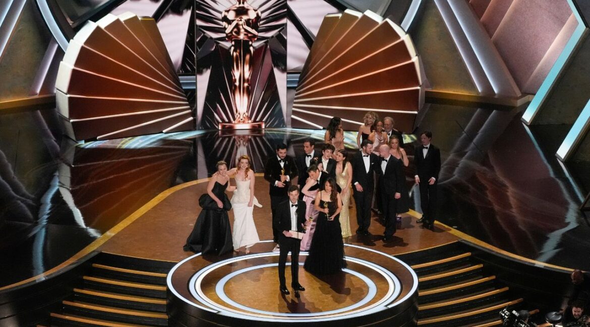 Daria Ekamasova, from left, Lindsey Normington, Vache Tovmasyan, Karren Karagulian, Alex Coco, front left, Samantha Quan, front right, Mikey Madison, Sean Baker, Mark Eydelshteyn, and Yura Borisov accept the award for best picture for "Anora" during the Oscars on Sunday, March 2, 2025, at the Dolby Theatre in Los Angeles. Meg Ryan and Billy Crystal look on from back of stage right.(AP Photo/Chris Pizzello)
