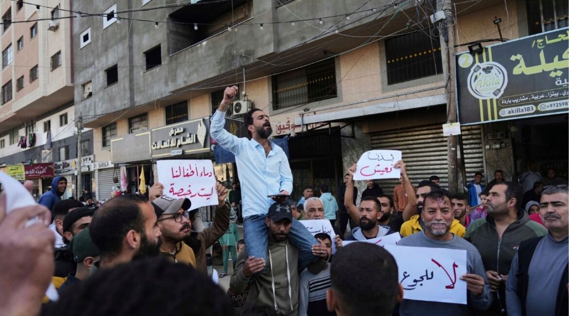 Palestinians hold signs against the war as a man chants slogans in support of the people in Bait Lahiya who came out against Hamas Tuesday in a rare show of public anger against the militant group that rules the territory, in Deir al-Balah, Gaza Strip, Wednesday, March 26, 2025. (AP/Abdel Kareem Hana)