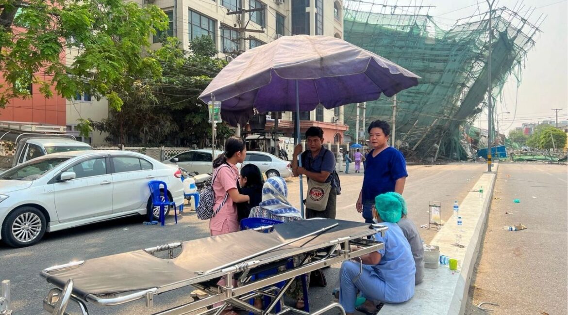 Medical personnel wait with an empty stretcher near a hospital in Mandalay, Myanmar, where a collapsed building and blocked streets could be seen in the distance after a 7.7-magnitude earthquake struck nearby on Friday, March 28, 2025. Bridges and buildings collapsed in Mandalay, with many casualties reported; the quake was strong enough to collapse a 30-story skyscraper under construction over 500 miles away, in Bangkok. (The New York Times)