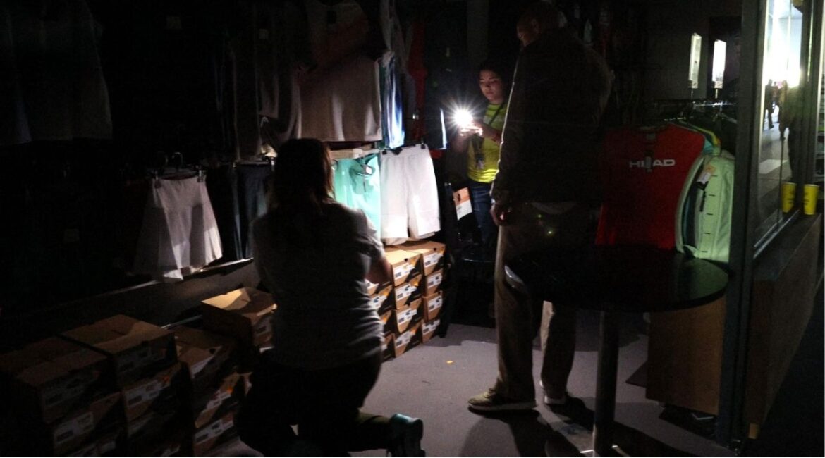 Tennis - Madrid Open - Park Manzanares, Madrid, Spain - April 28, 2025 People use their cell phone's flashlight in a dark sports shop after the matches get suspended due to a power outage (REUTERS/Violeta Santos Moura)