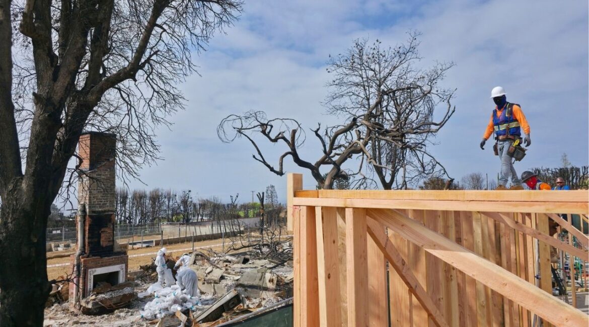A worker stands atop a home being rebuilt after the Palisades Fire in the Pacific Palisades neighborhood of Los Angeles, Thursday, April 24, 2025. (AP Photo/Damian Dovarganes)