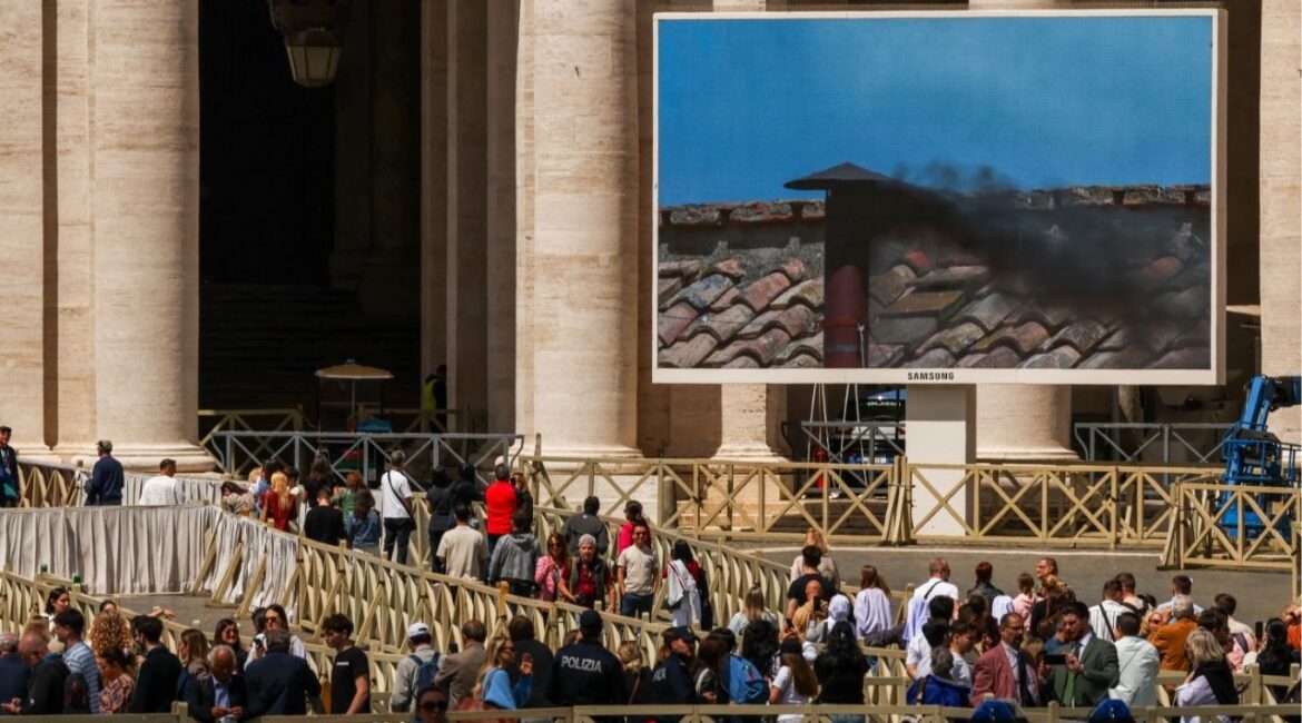 People watch as a screen shows black smoke rising from the chimney on the Sistine Chapel, indicating no decision has been made to elect a new pope, as seen from Rome, Italy May 8, 2025. REUTERS/Alkis Konstantinidis