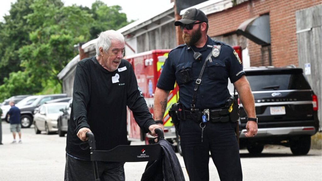 A resident of Gabriel House Assisted Living Facility is assisted by a Fall River police officer outside an emergency shelter set up at the Timao Center, after a deadly fire broke out in Fall River, Massachusetts, U.S. July 14, 2025. (Reuters/Ken McGagh)