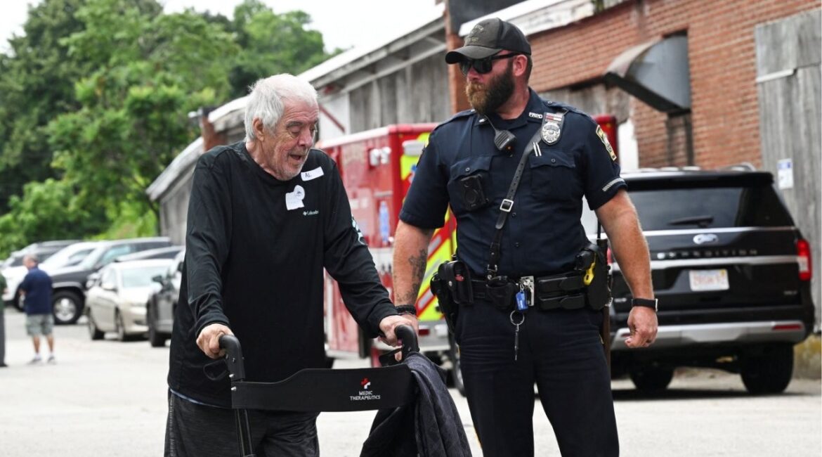 A resident of Gabriel House Assisted Living Facility is assisted by a Fall River police officer outside an emergency shelter set up at the Timao Center, after a deadly fire broke out in Fall River, Massachusetts, U.S. July 14, 2025. (Reuters/Ken McGagh)