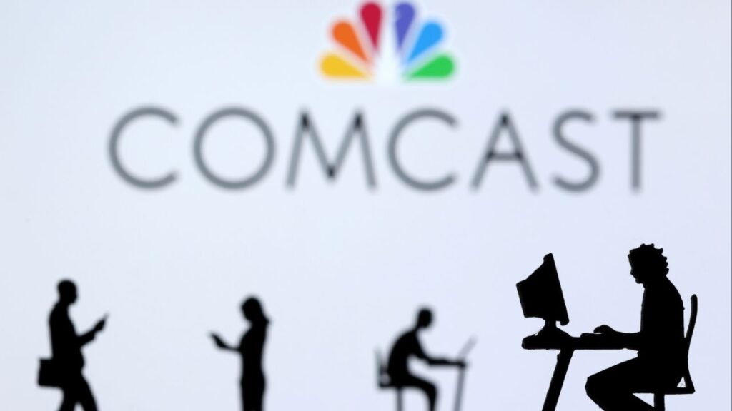 Small toy figures with laptops and smartphones are seen in front of displayed Comcast logo, in this illustration taken December 5, 2021. (Reuters File)