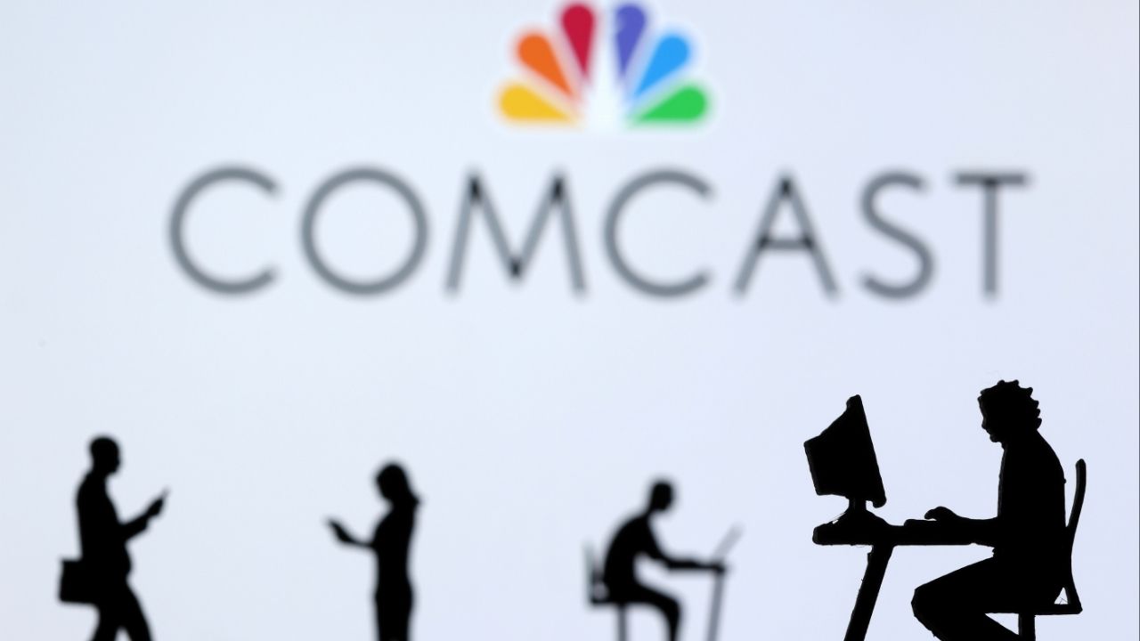 Small toy figures with laptops and smartphones are seen in front of displayed Comcast logo, in this illustration taken December 5, 2021. (Reuters File)