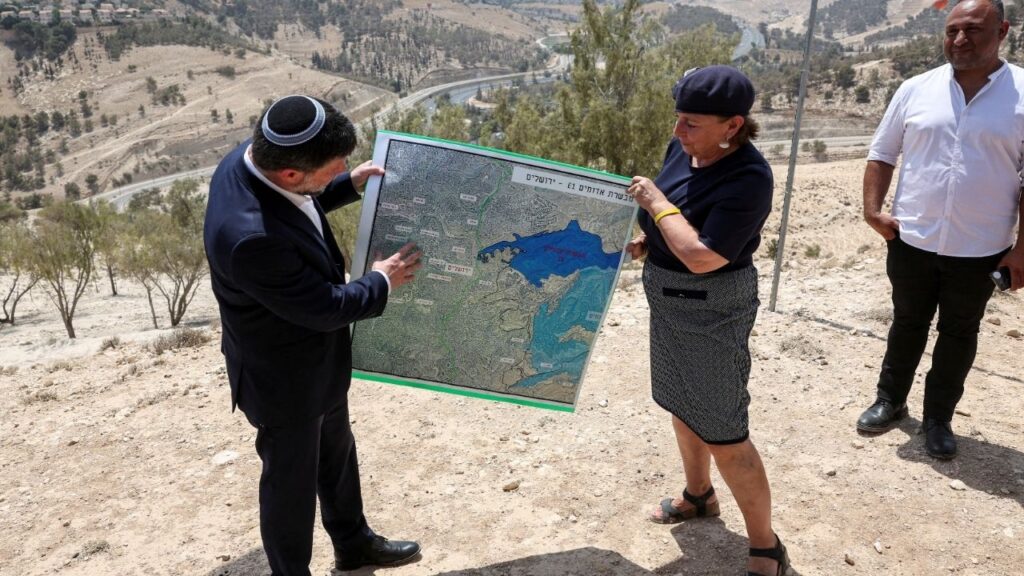 Israeli Finance Minister Bezalel Smotrich and a woman hold a map that shows the long-frozen E1 settlement scheme, that would split East Jerusalem from the occupied West Bank, on the day of a press conference near the Israeli settlement of Maale Adumim, in the Israeli-occupied West Bank, August 14, 2025. (Reuters File)